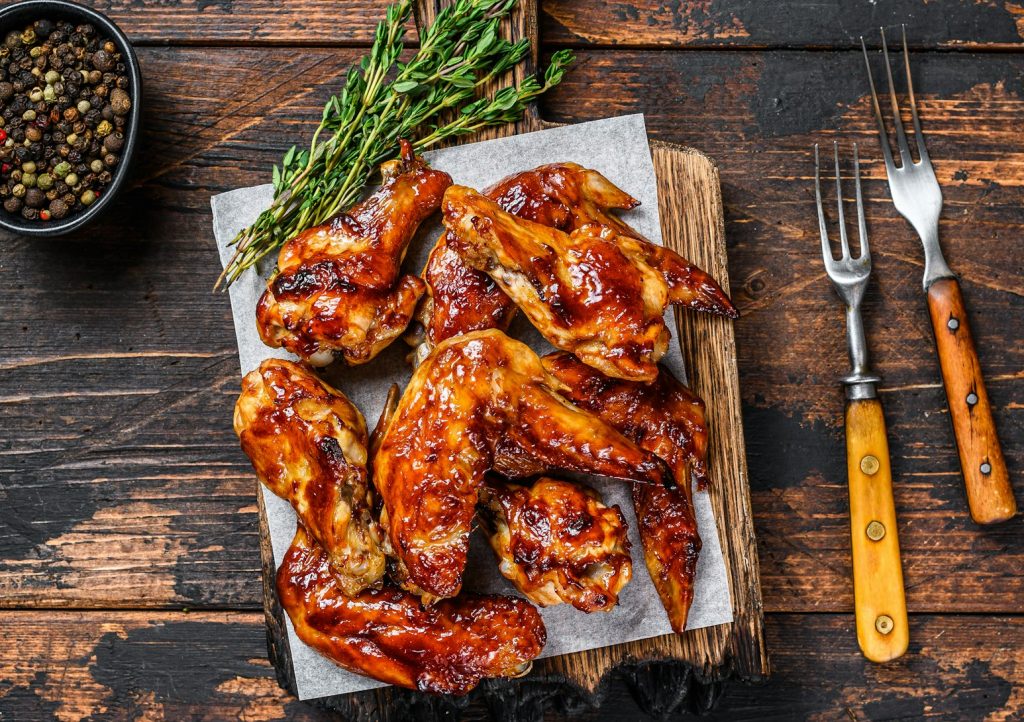 Baked Bbq chicken wings with dip sauce. Dark wooden background. Top view