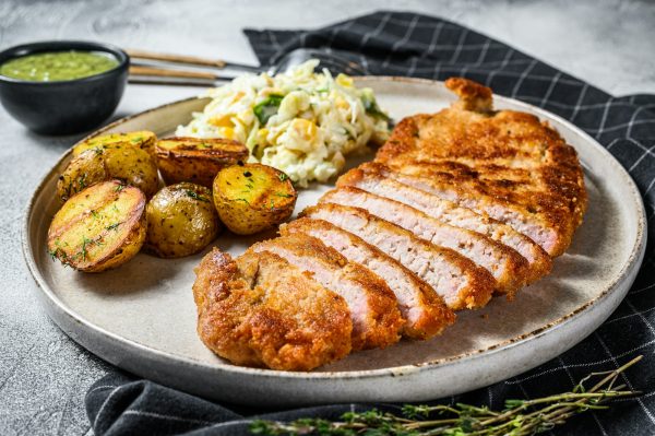 Breaded viennese schnitzel with baked potatoes and salad. Gray background. Top view