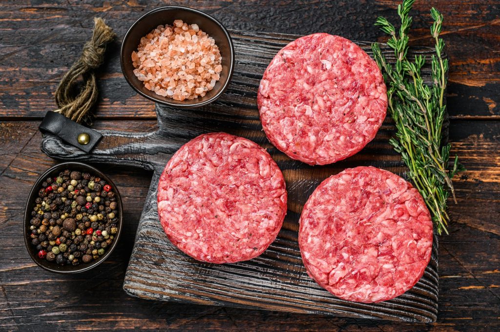 Raw steak burgers patties with ground beef and thyme on a wooden cutting board.